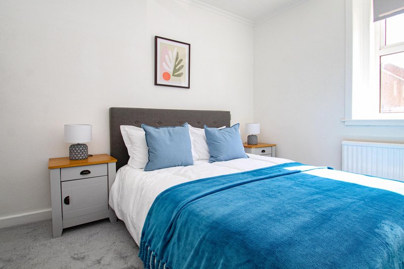 Bright bedroom with double bed, blue bedding, grey headboard, and white bedside table