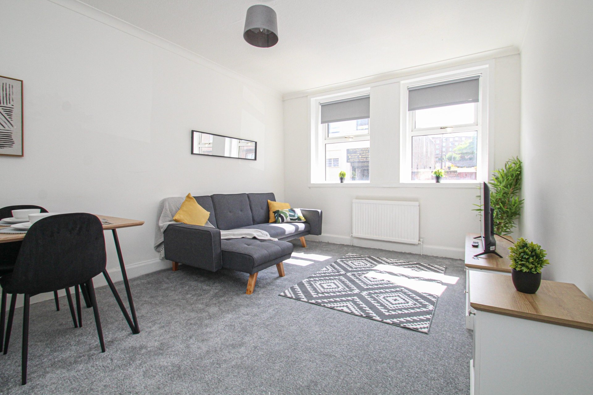 Modern living room with gray sofa, dining table, chair, plants and large windows