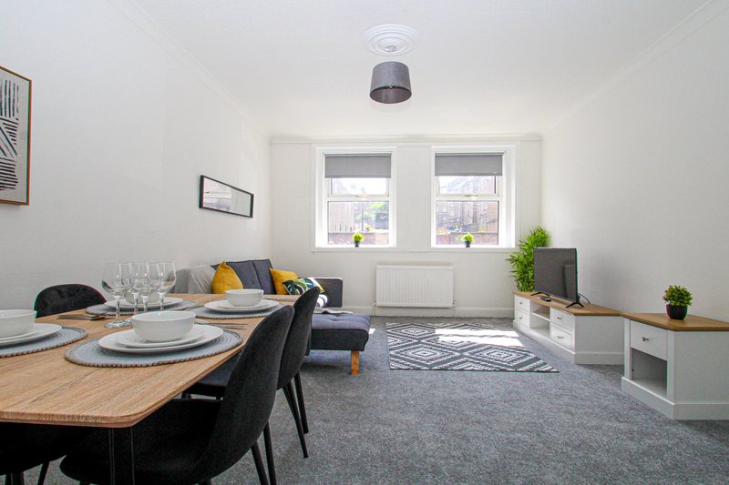 Open-plan living and dining area with wooden table, black chairs, grey sofa, and large windows