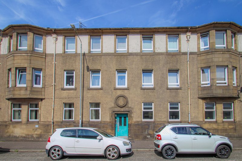 Stone tenement building with turquoise door, parked cars on street, blue sky