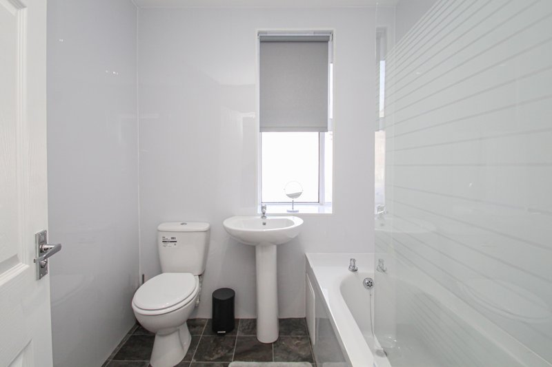 Compact bathroom with toilet, pedestal sink, bathtub and window with roller blind