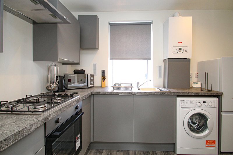 Modern kitchen with gray cabinets, gas hob, washing machine and granite countertop