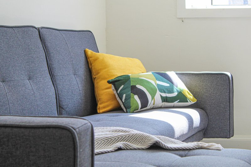 Gray upholstered sofa with yellow and patterned cushions and striped throw blanket
