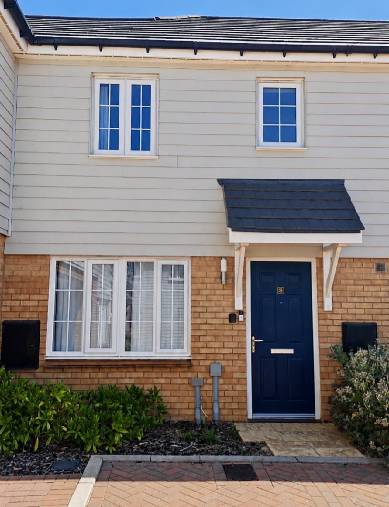 Modern two-story townhouse exterior with brick and rendered facade, navy door and windows