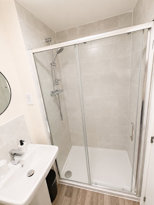 Clean modern bathroom with white basin, shower enclosure and wooden-effect flooring