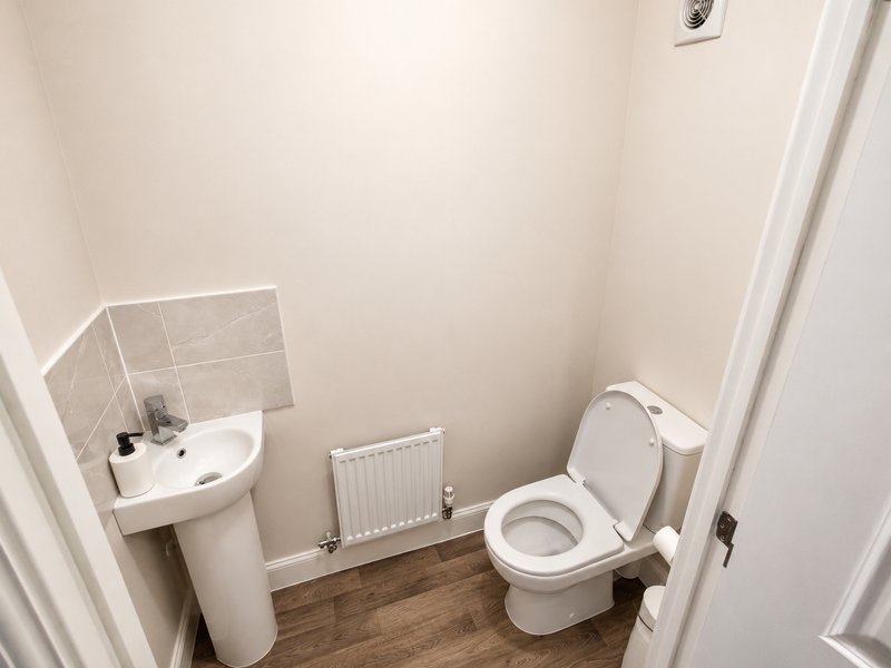 Small bathroom with pedestal sink, toilet, radiator and tiled splashback