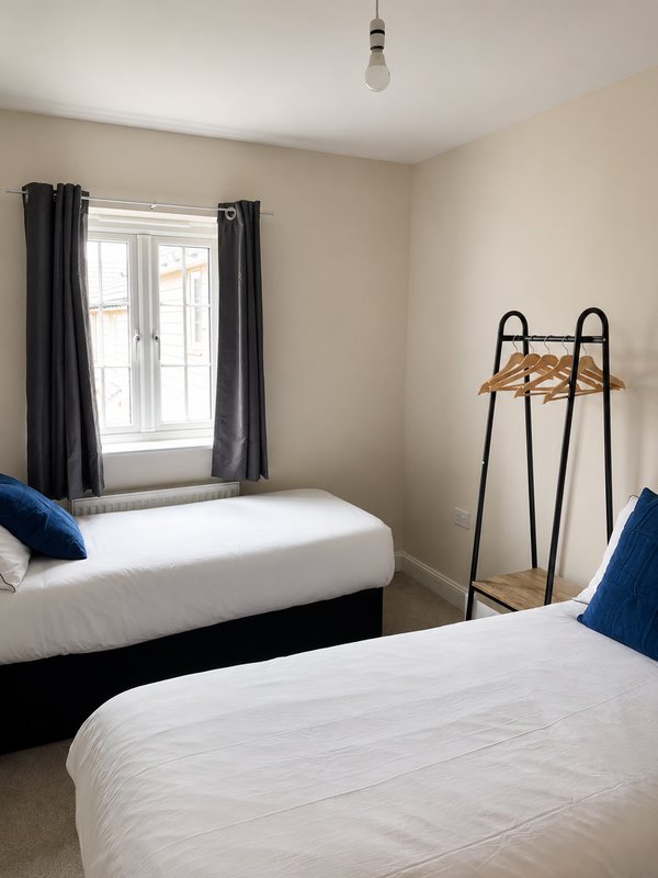 Twin bedroom with two single beds, black curtains, window with countryside view, luggage rack