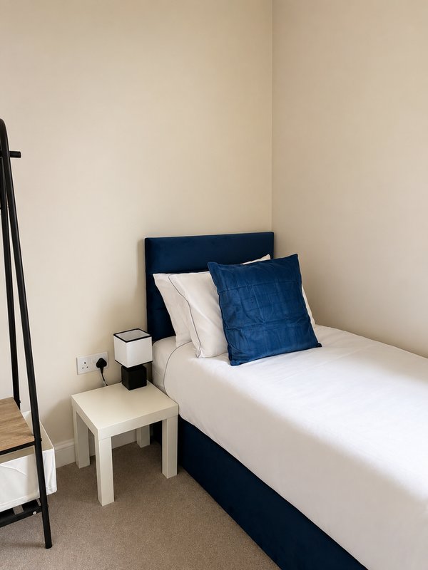 Bedroom with navy blue bed frame, white bedding, blue cushion, and small wooden nightstand