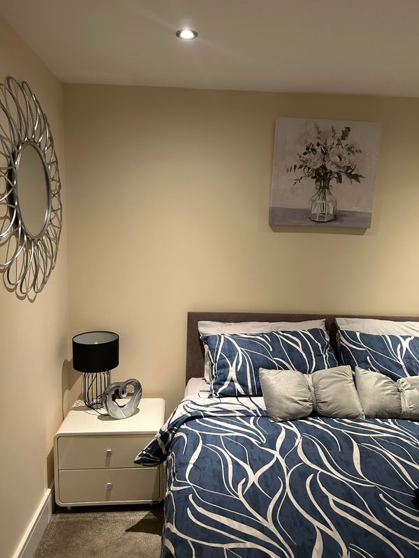 Bedroom with double bed, navy patterned bedding, white nightstand, decorative wall art and lighting