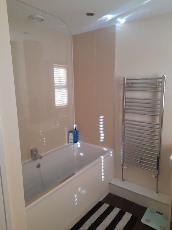 Modern bathroom with bath, glass shower screen, heated towel rail and striped floor mat