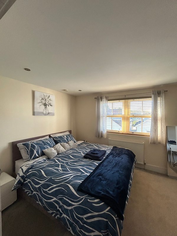 Bright bedroom with double bed, patterned bedding, wall art, and large window with blinds