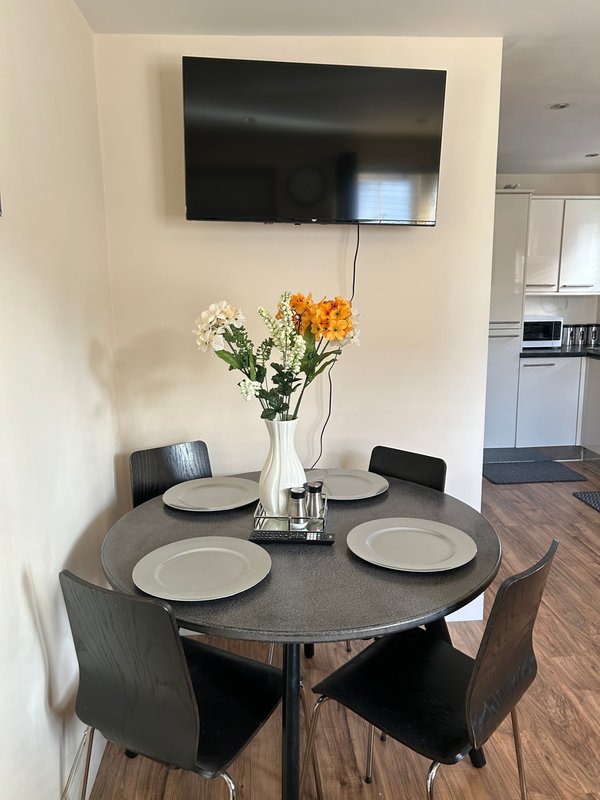 Dining area with round table, four chairs, place settings, and fresh flowers in vase