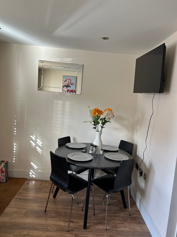 Modern dining area with black round table, four chairs, flowers and wall-mounted TV