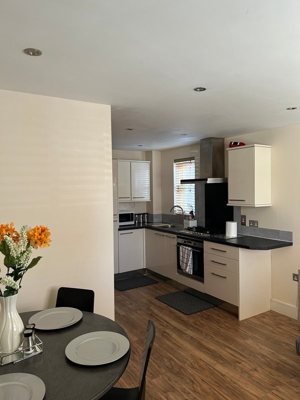 Modern kitchen with cream cabinetry, black countertop, and dining table with flowers in foreground