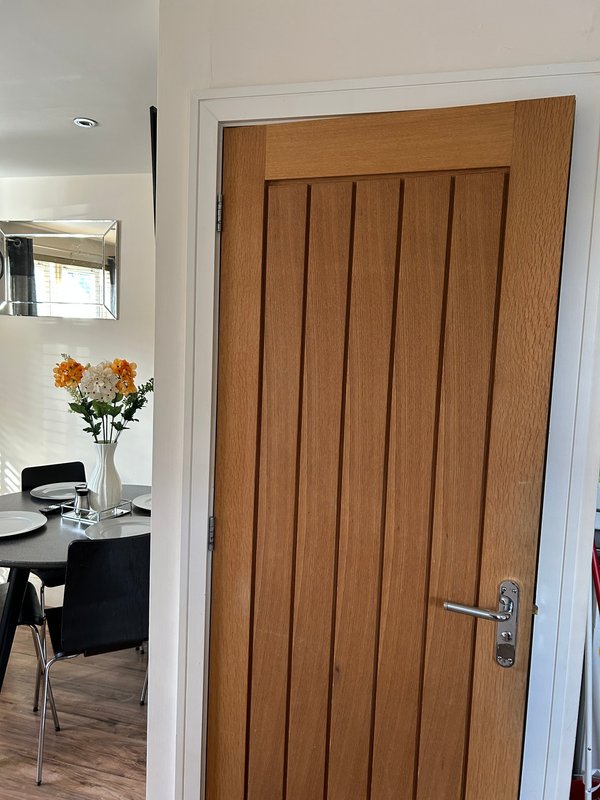 Interior hallway with wooden door, white walls, mirror, and flowers in vase