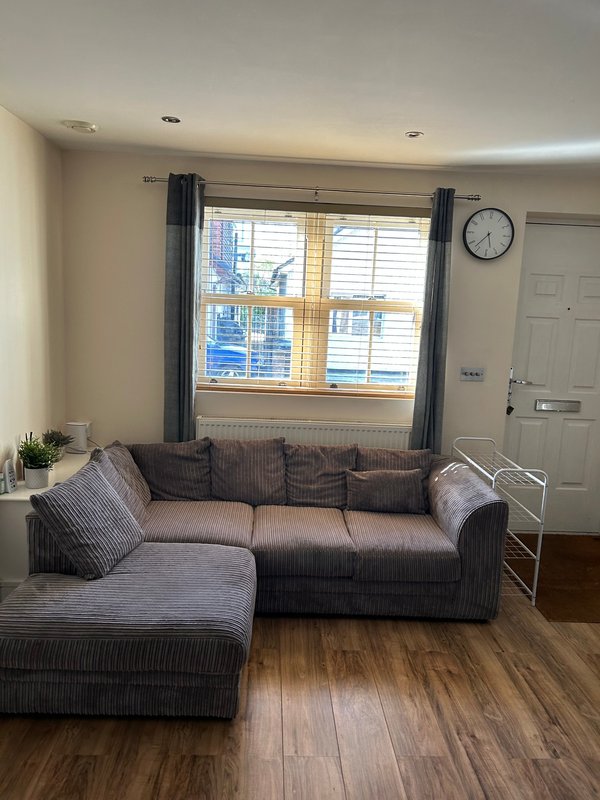 Living room with gray corner sofa, cushions, wooden floor and large window with curtains