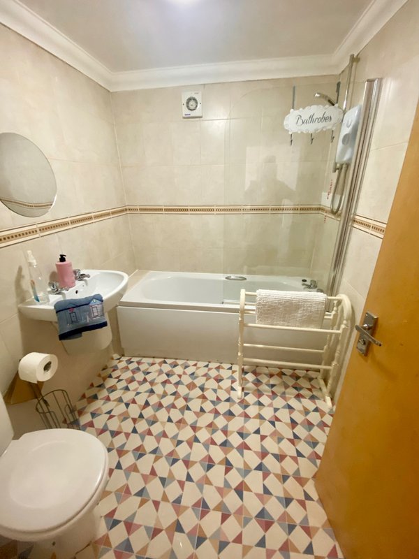 Bathroom with toilet, bathtub, sink, geometric floor tiles and white wall paneling