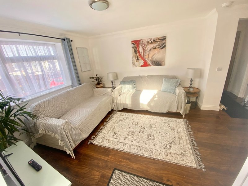 Bright bedroom with double bed, cream sofa, wooden floor, and framed wall art