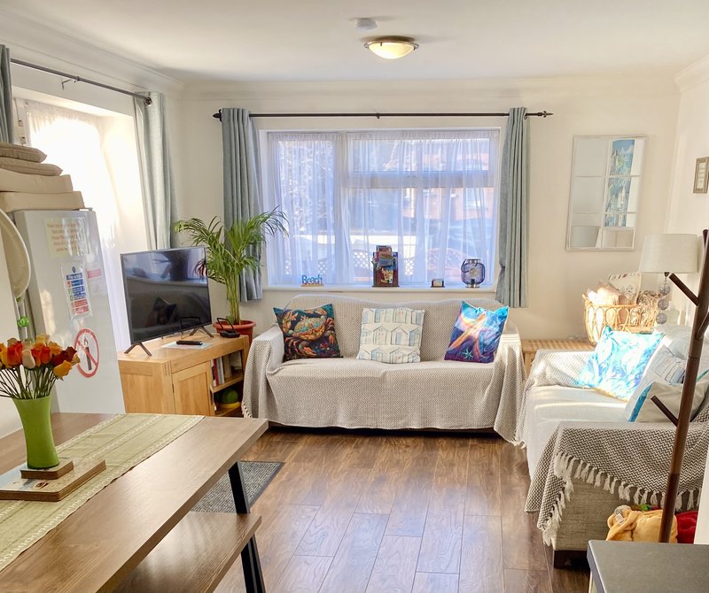 Bright living room with sofa, armchair, TV, wooden furniture, large windows with curtains