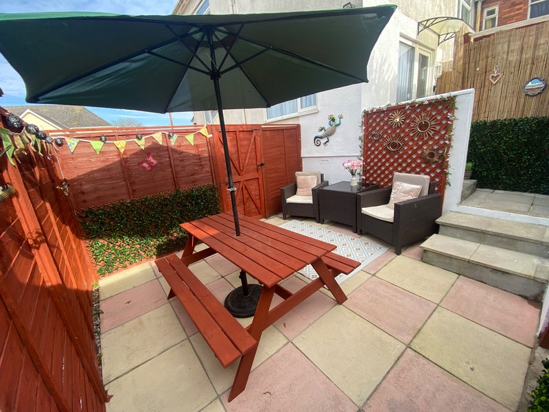 Outdoor garden patio with red picnic table, black umbrella, rattan seating and wooden fencing