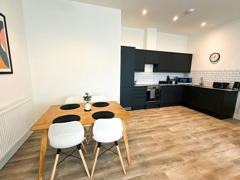 Open-plan kitchen and dining area with wooden table, white chairs, dark cabinetry and brick backsplash