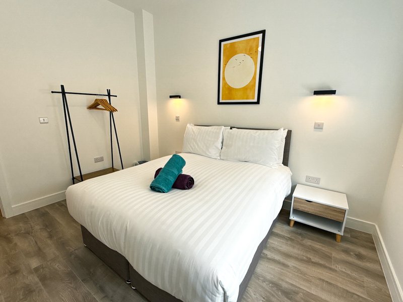 Modern bedroom with double bed, white bedding, wooden flooring and wall art