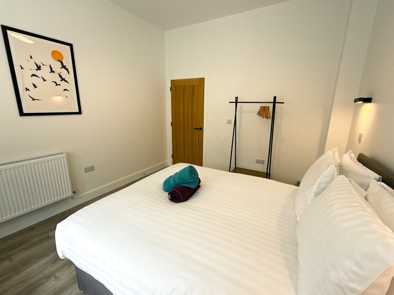 Bedroom with double bed, white bedding, wooden door, wall art and radiator