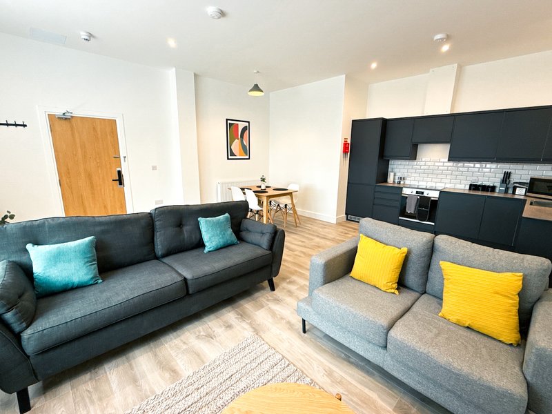Open-plan living area with two sofas, wooden flooring, kitchenette and dining table