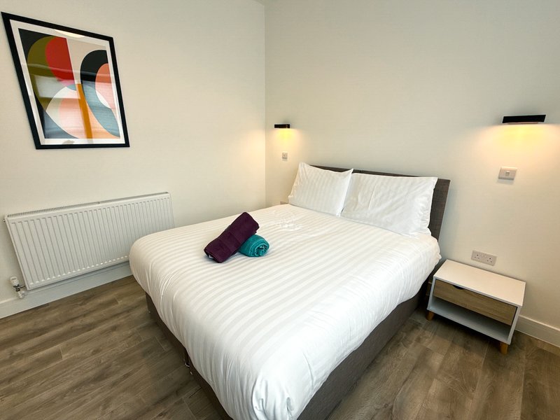 Modern bedroom with double bed, white bedding, bedside lamps, radiator and framed wall art