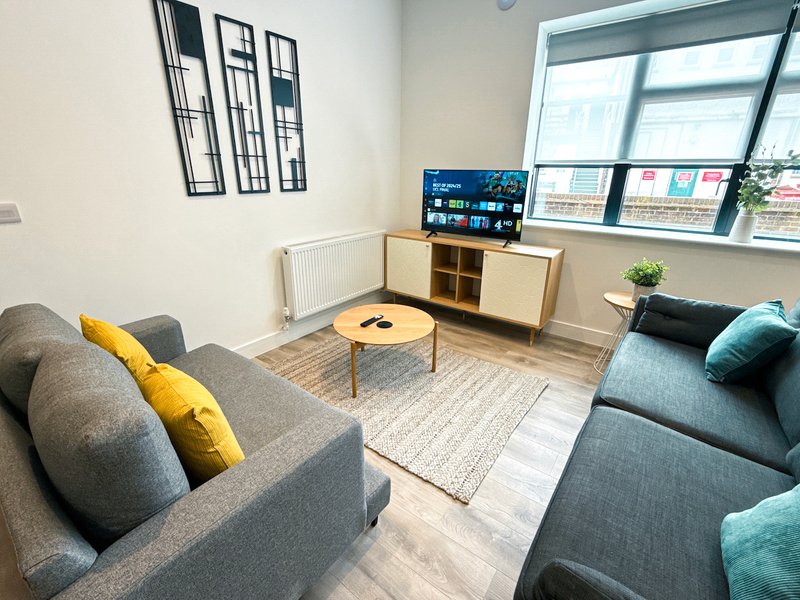 Modern living room with grey sofas, wooden coffee table, TV on stand, and large windows