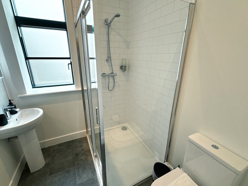 Modern bathroom with pedestal sink, walk-in shower, toilet, and window