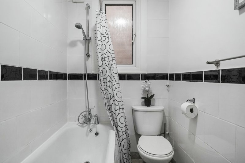 Small bathroom with white tiles, bathtub, toilet, shower head and patterned curtain