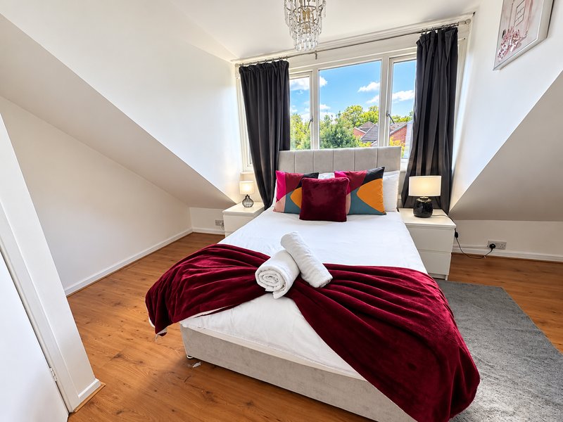 Bright attic bedroom with double bed, burgundy velvet throw, colorful cushions and large window