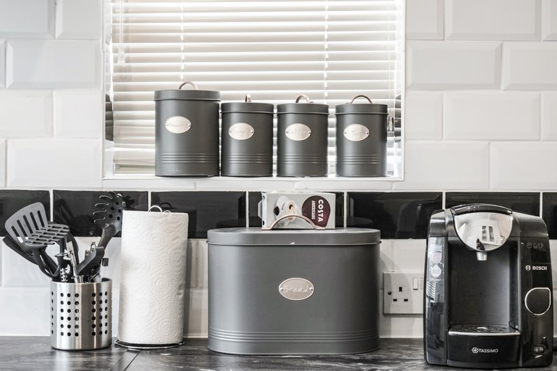Kitchen counter with black appliances, storage canisters, utensil holder, and white window blinds