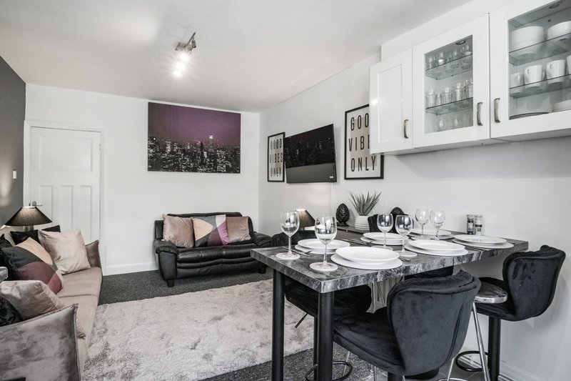 Modern open-plan living and dining area with black sofa, dining table, and kitchen cabinets