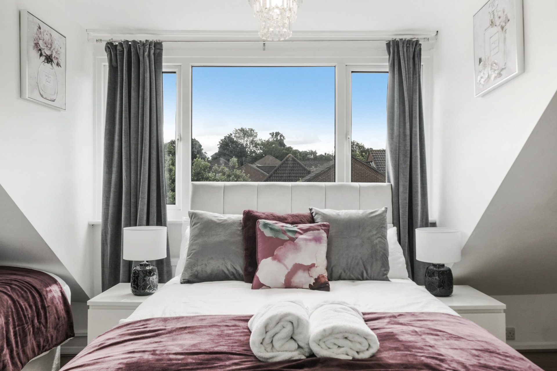 Modern bedroom with double bed, rolled towels, grey curtains and large window with garden view