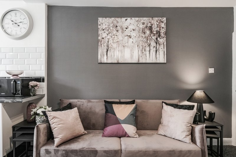 Modern living room with gray sofa, decorative pillows, wall art, and wall clock