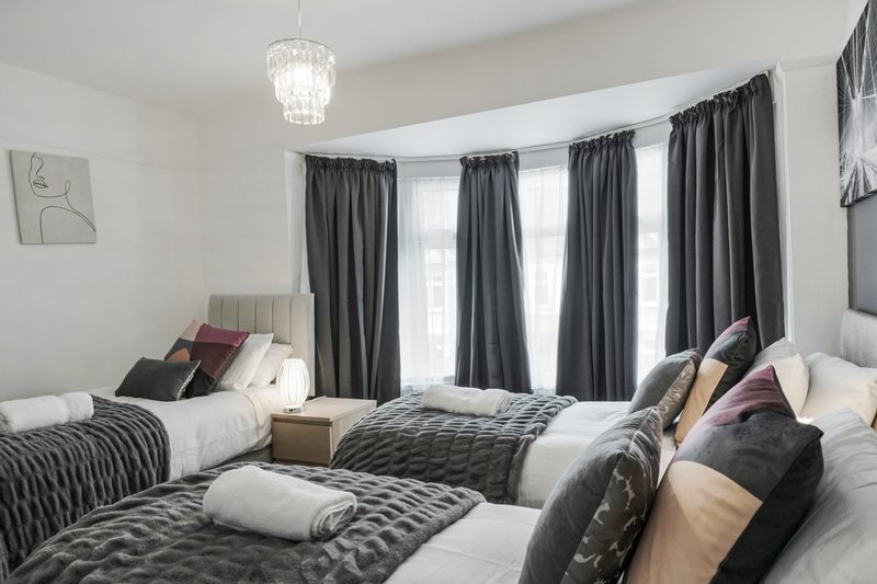 Bright bedroom with two beds, dark curtains, pendant light and cushions