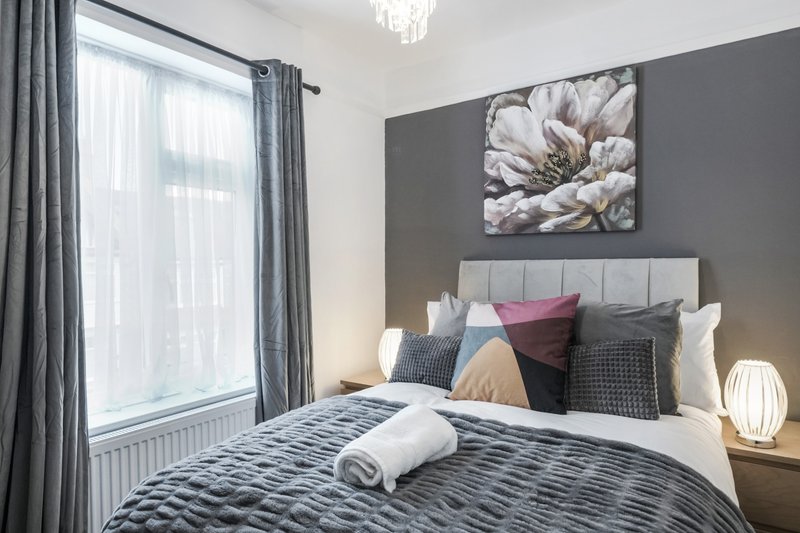 Modern bedroom with double bed, gray headboard, patterned bedding, and floral wall art