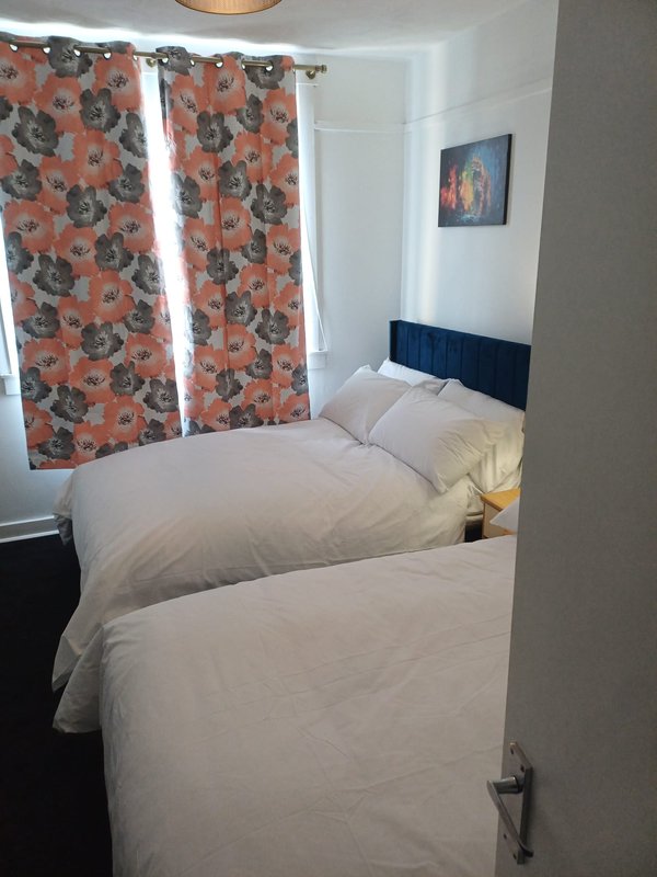 Bedroom with two single beds, patterned orange curtains, and wall-mounted artwork