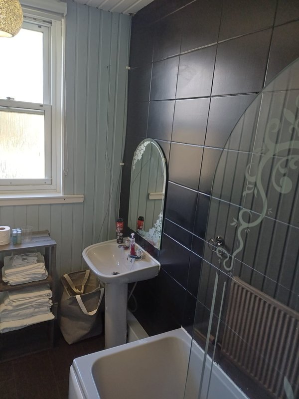 Bathroom with pedestal sink, mirror, black tile wall and window with natural light