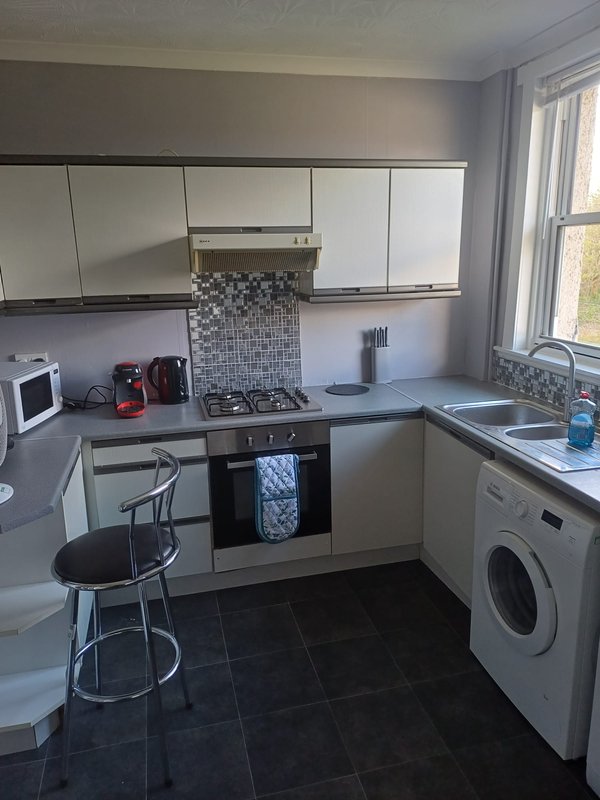 Modern kitchen with white cabinetry, gas hob, washing machine and breakfast bar seating