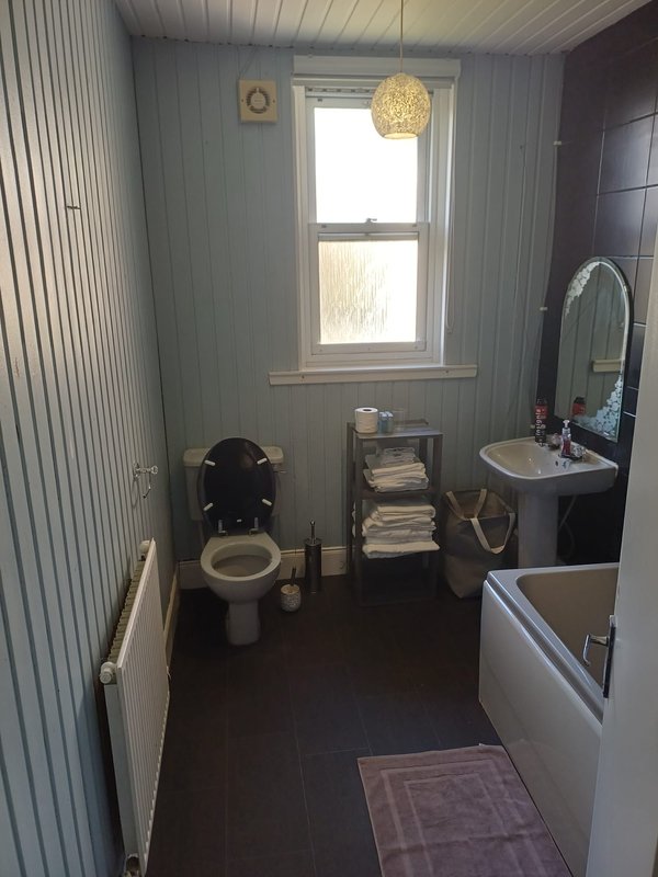 Small bathroom with toilet, sink, mirror, window and towel storage shelving