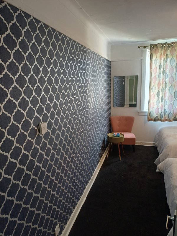Bedroom with patterned navy wallpaper, twin beds, small table, and window with curtains