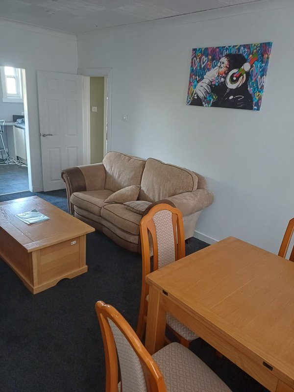 Living room with beige sofa, wooden dining table, chairs, and wall art