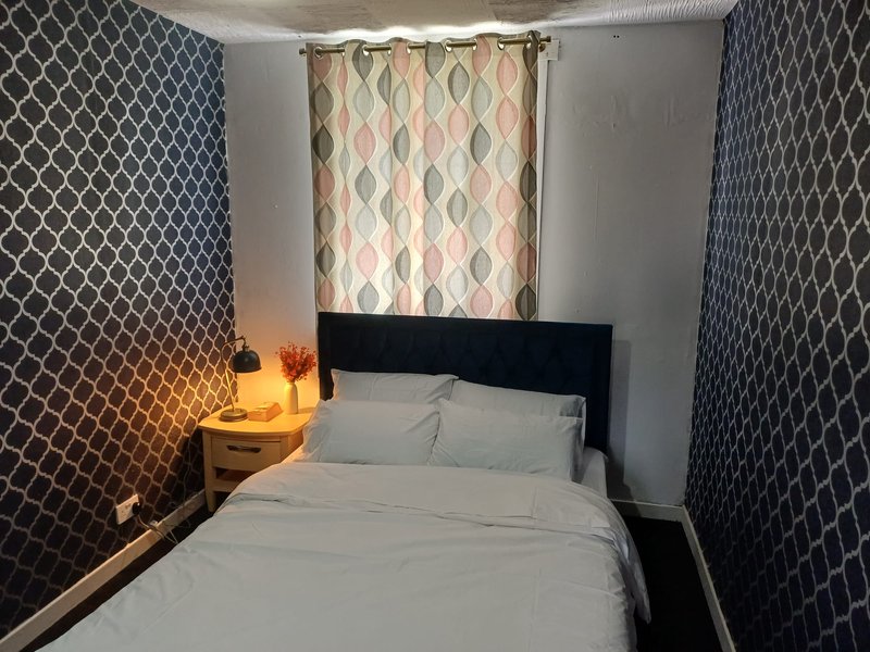 Small bedroom with double bed, black headboard, patterned wallpaper, bedside lamp and window