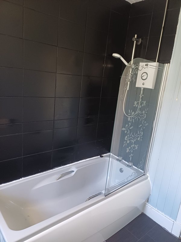 Modern bathroom with white bathtub, black tile walls, and glass shower enclosure
