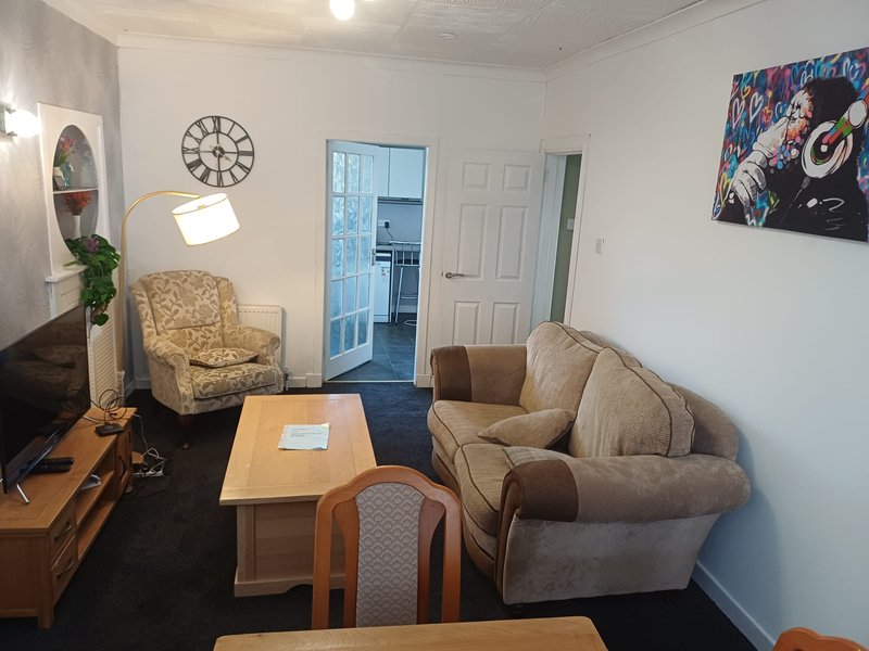 Open-plan living room with upholstered seating, wooden coffee table, wall clock and framed artwork