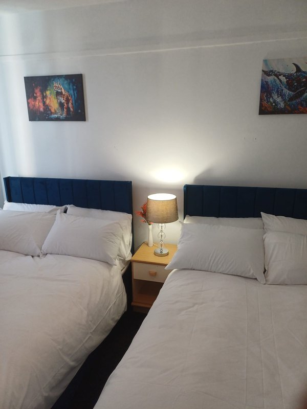 Bedroom with two double beds, blue headboards, white bedding, wooden nightstand and wall art