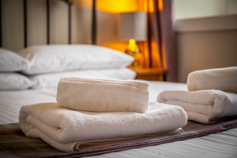 Bedroom with folded white towels on bed, pillows and warm lighting
